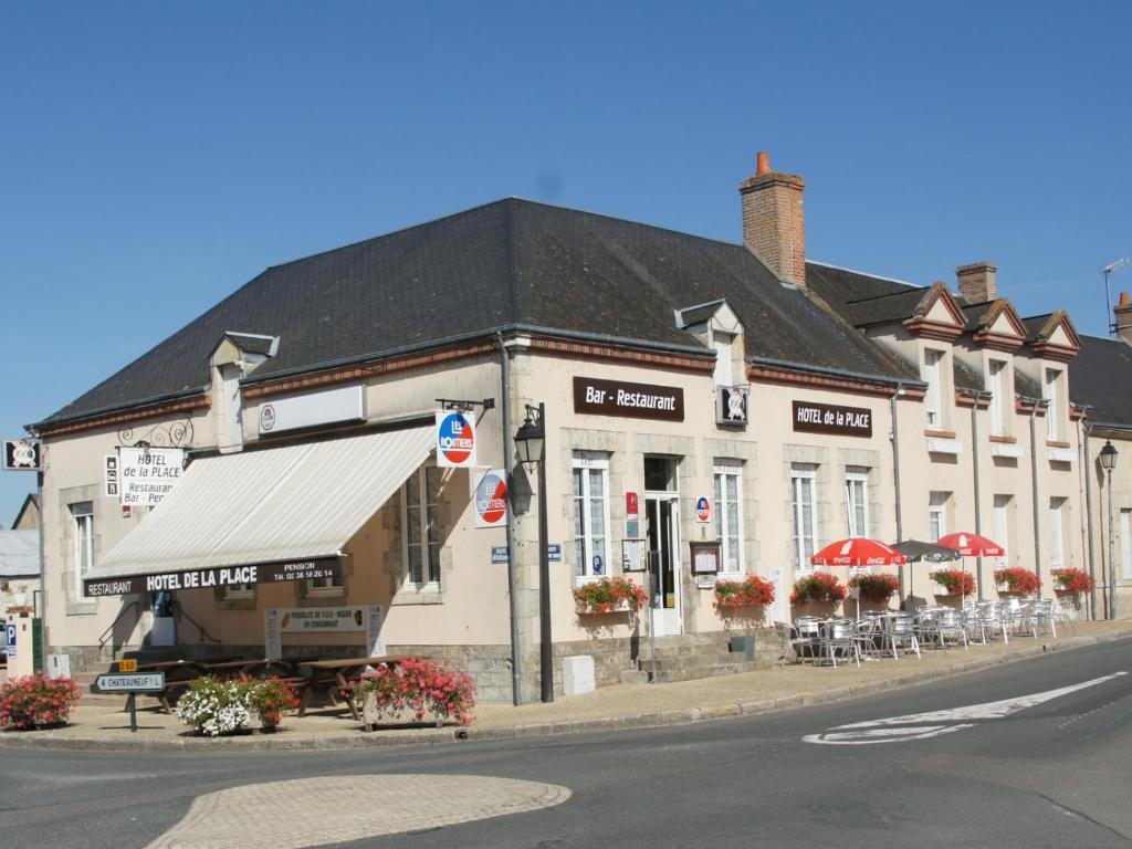 un grand bâtiment blanc avec des tables et des chaises dans une rue dans l'établissement Hôtel de la Place, à Germigny-des-Prés