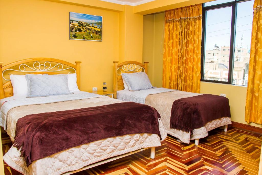Duas camas num quarto com paredes amarelas e uma janela. em Rayos Del Sol em Juliaca