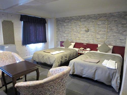 a hotel room with two beds and a table and chairs at Hotel Rumieru Hyuga in Hyuga
