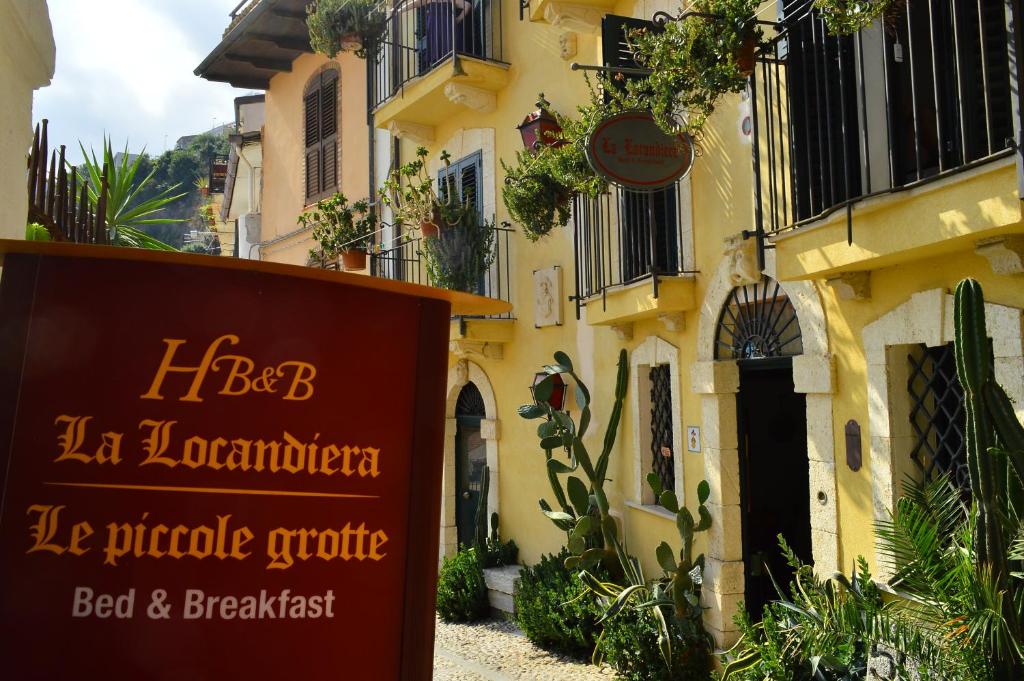 a sign in front of a building with plants at La Locandiera affittacamere in Scilla