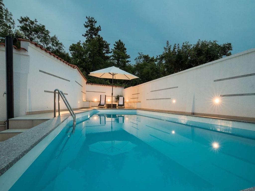 a swimming pool with an umbrella next to a white wall at Apartment Villa Zdenka in Crikvenica