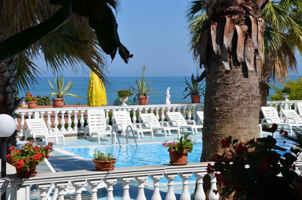 a swimming pool with white chairs and a palm tree at Camping Terrazzo sul mare in Cupra Marittima