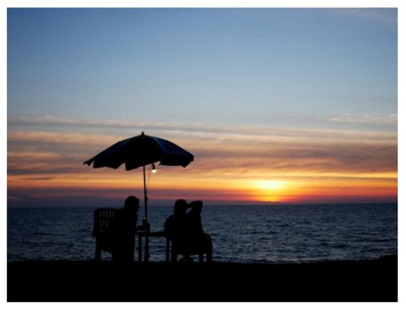 Micky Monkey Beach Hotel Phuket Maikhao Thailand في شاطئ ماي خاو: يجلس شخصان على طاولة تحت مظلة على الشاطئ