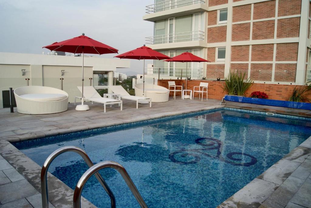 una piscina con sillas y sombrillas junto a un edificio en Hotel Velvet Plaza, en Guadalajara