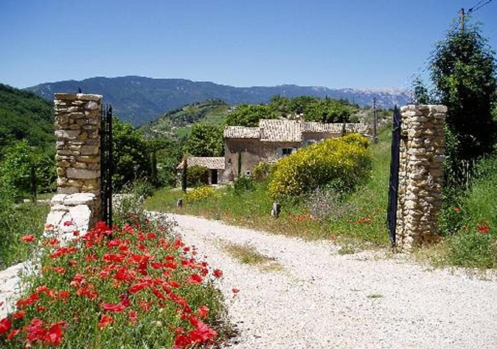 un chemin de terre avec des fleurs rouges et un bâtiment dans l'établissement La Maison de Marguerite, à Montbrun-les-Bains