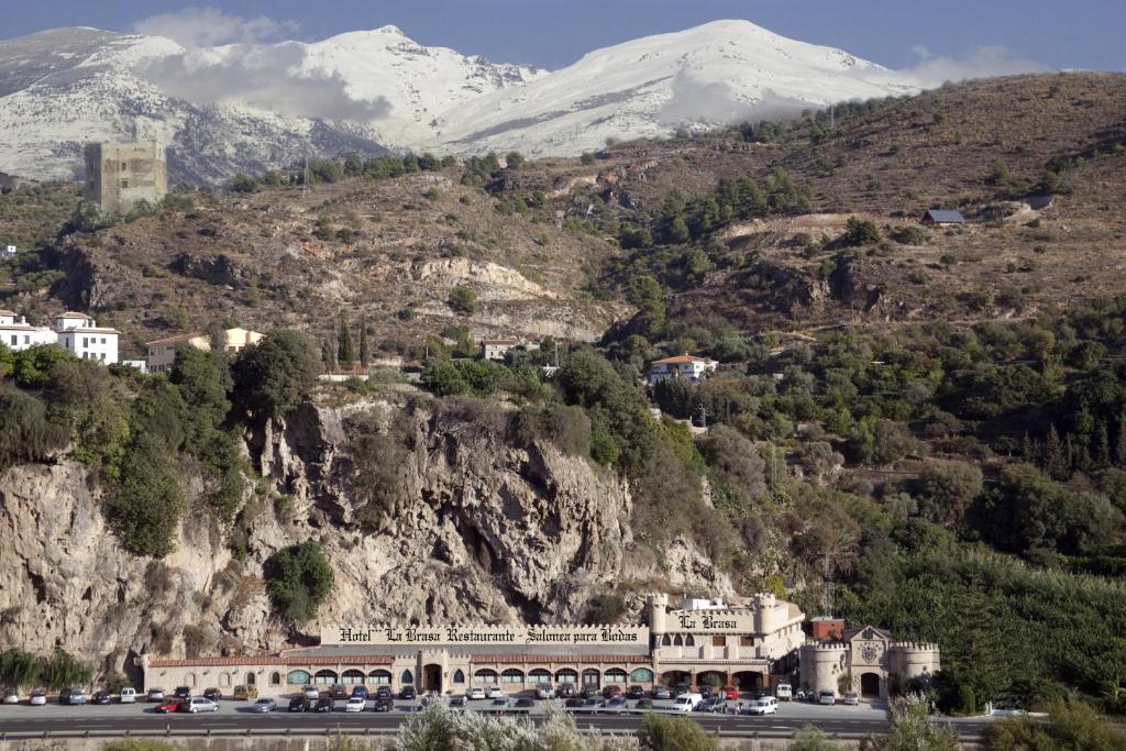 a building on a mountain with snow covered mountains in the background at Hotel La Brasa in Vélez de Benaudalla