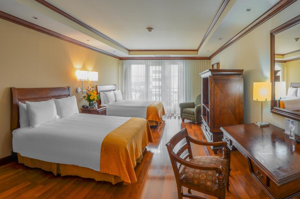 a hotel room with two beds and a desk and a television at Hotel Casa Veranda Guatemala in Guatemala