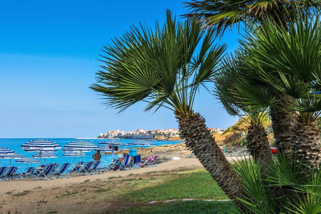 una spiaggia con sedie, palme e l'oceano di Hotel Poseidon a Diamante