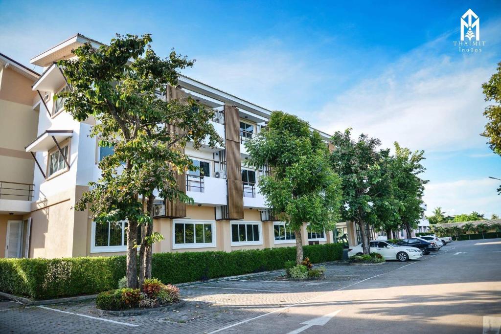 an apartment building with trees in a parking lot at Thaimit Resort in Uttaradit