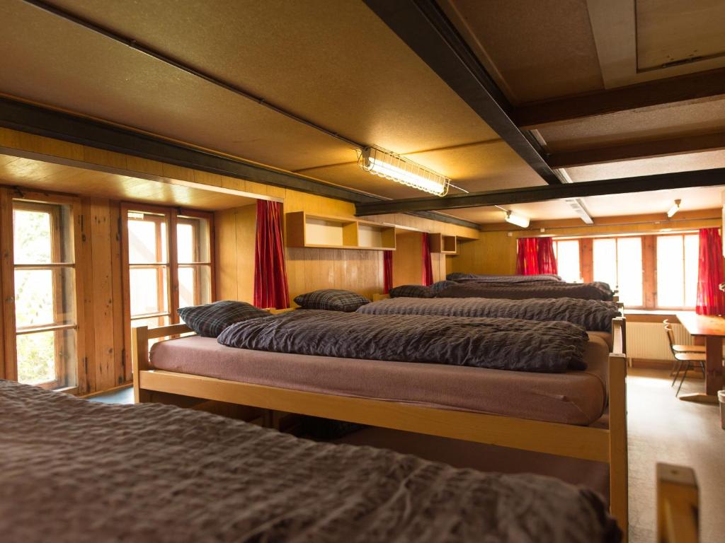 eine Reihe von Betten in einem Zimmer mit Fenstern in der Unterkunft Gasthaus Pension zum Turm in Hospental
