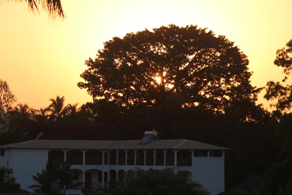 a building with the sun setting behind a tree at Casa Motel in Ziguinchor