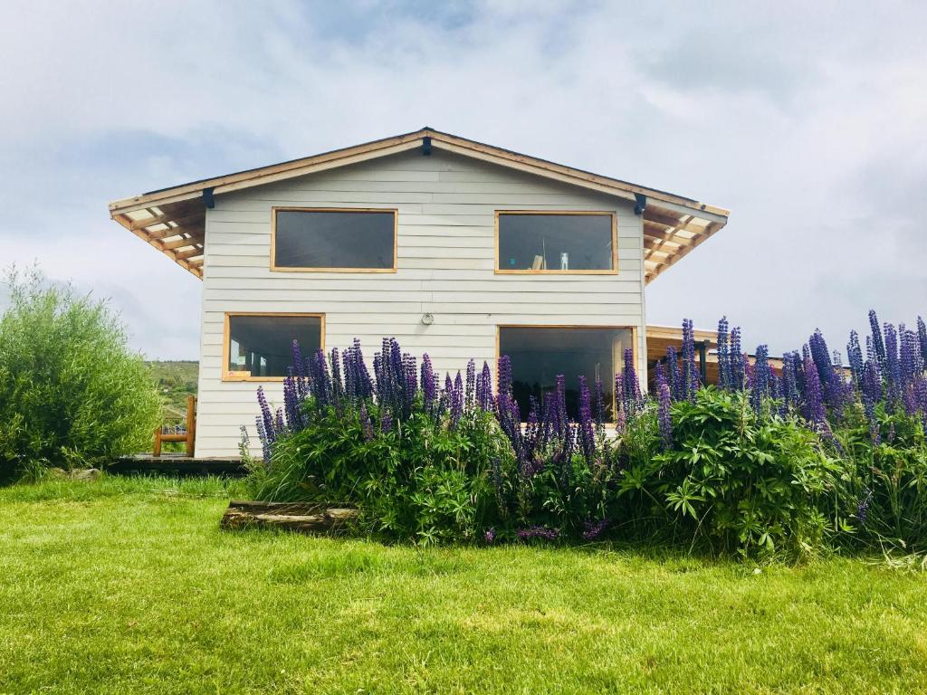 una casa con flores púrpuras delante de ella en Piuke Mapu Patagonia Hostel en Cholila