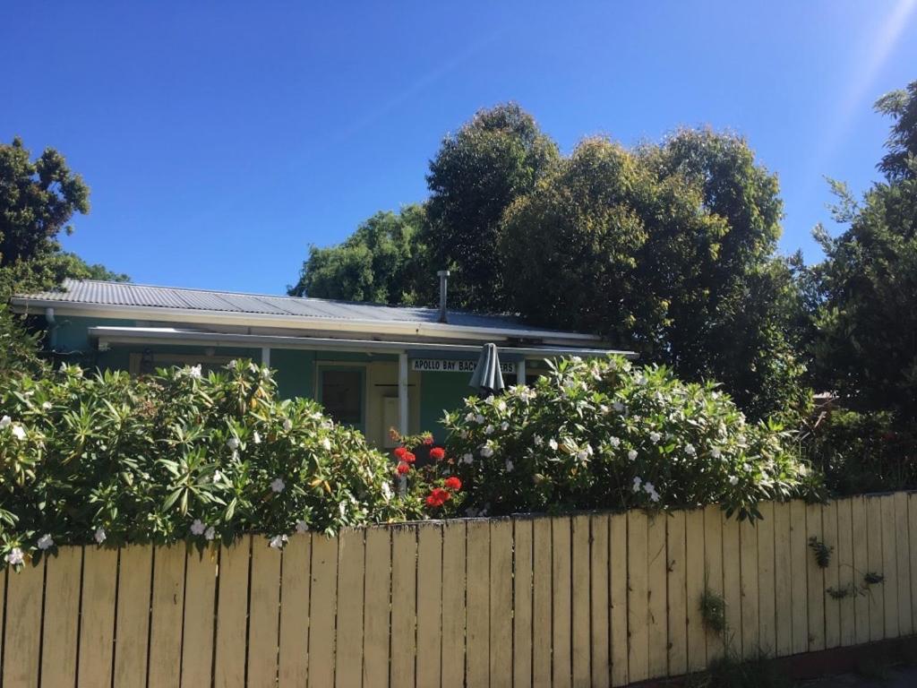 a house behind a fence with bushes and flowers at Apollo Bay Backpackers in Apollo Bay
