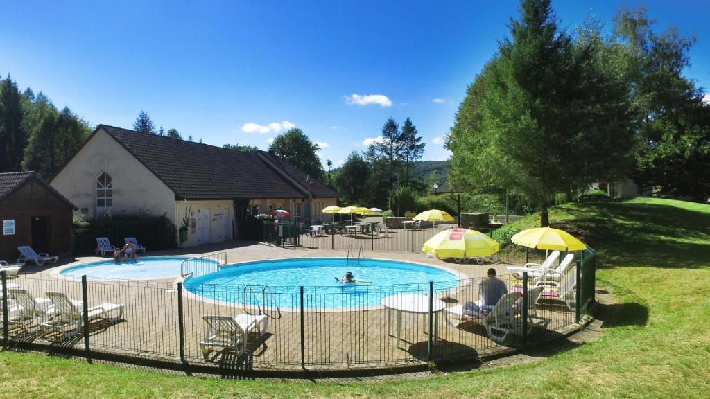 una piscina con sillas y sombrillas en un patio en VVF Cantal Champs-sur-Tarentaine, en Champs Sur Tarentaine