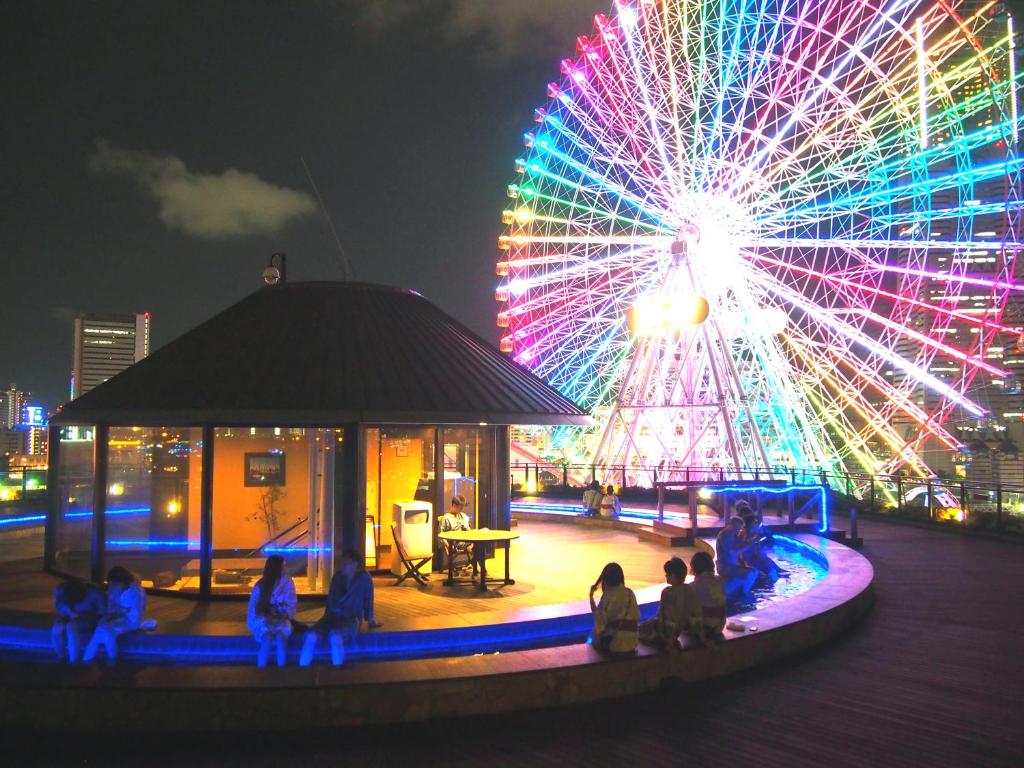 Una noria con gente sentada frente a ella. en Yokohama Minatomirai Manyo Club en Yokohama