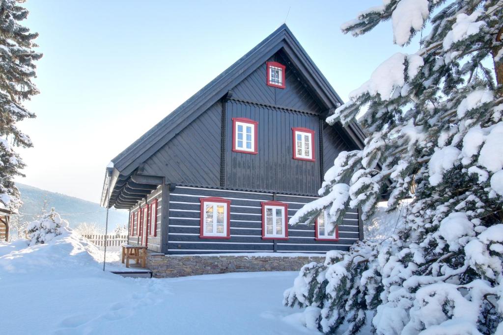 ein schwarzes Haus mit roten Fenstern im Schnee in der Unterkunft Chalupa U smrku in Horní Maršov