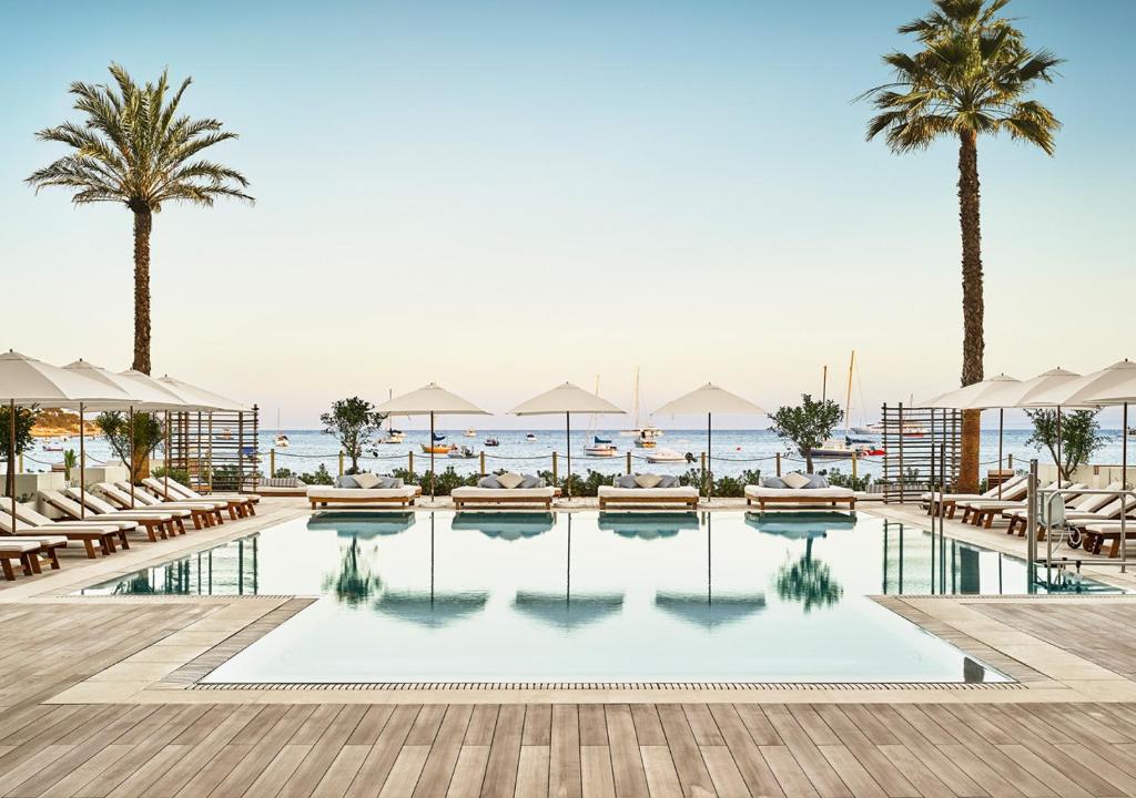 a pool with chairs and palm trees and the ocean at Nobu Hotel Ibiza Bay in Talamanca