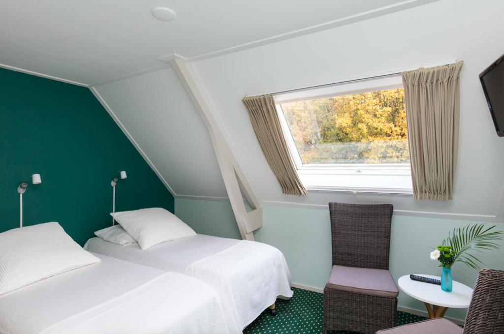 twee bedden in een kamer met een raam en een stoel bij De Herberg van Anderen in Anderen