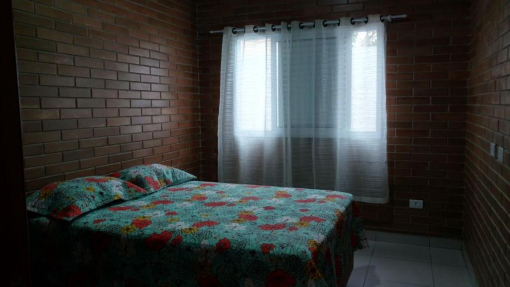 Cama en habitación de ladrillo con ventana en Chales Ilhabela ll, en Ilhabela