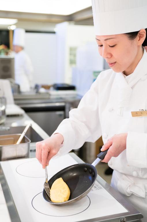 a chef is cooking food in a frying pan at Hotel Granvia Osaka-JR Hotel Group in Osaka