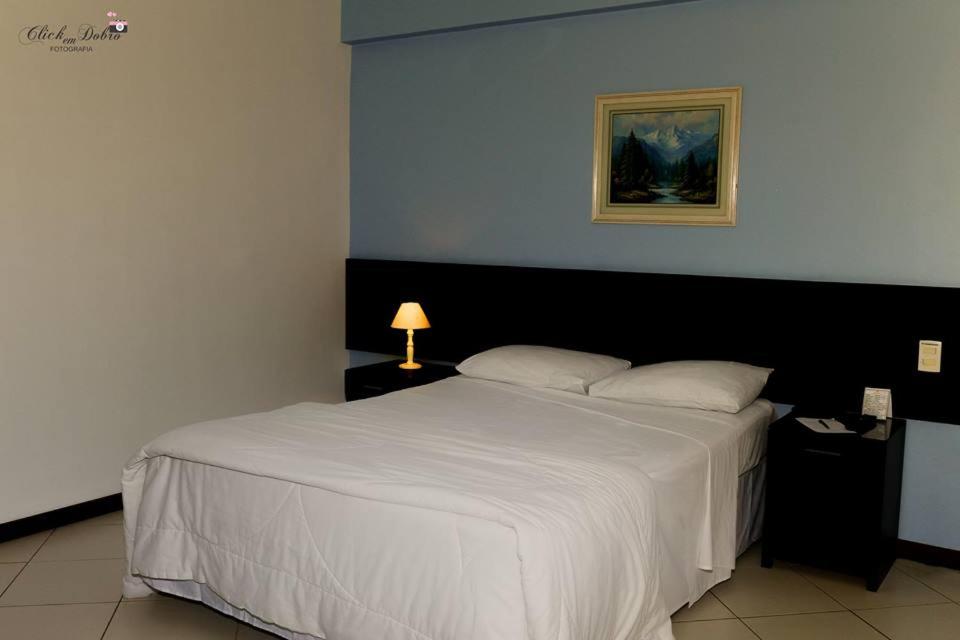 um quarto com uma grande cama branca e um candeeiro em Crystal Apart Hotel em Macaé
