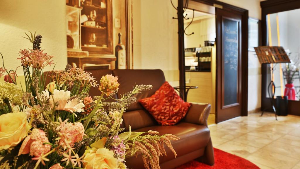 a living room with a brown couch and flowers at Hotel Restaurant Ruppert in Walluf