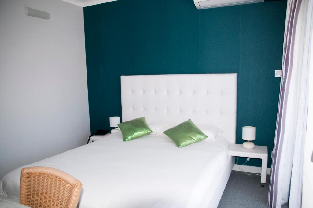 a bedroom with a white bed with two green pillows at Hotel Bleu Azur in Argelès-sur-Mer