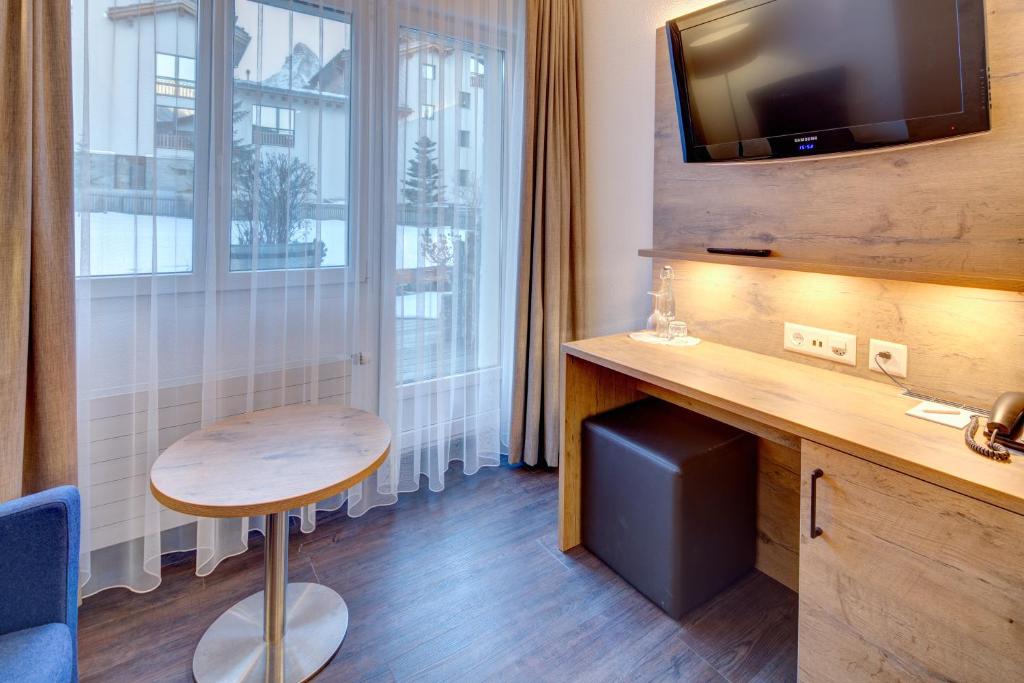 ツェルマットにあるAlpen Resort & Spaのデスク、テーブル、窓が備わる客室です。