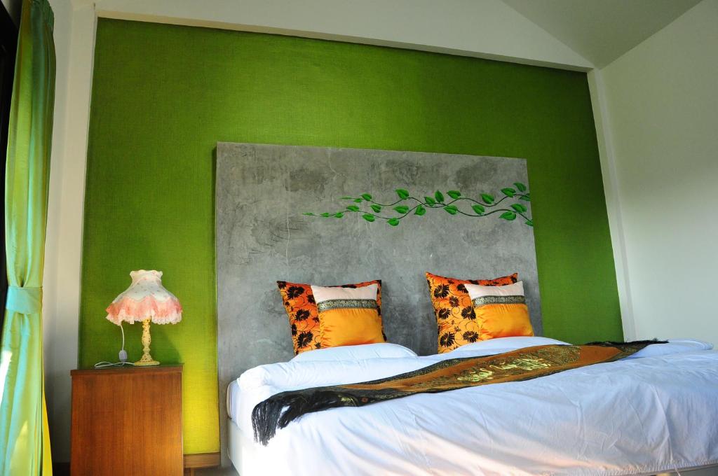 Un dormitorio con una pared verde y una cama con almohadas en Phumimalee Nature View Resort, en Nakhon Ratchasima