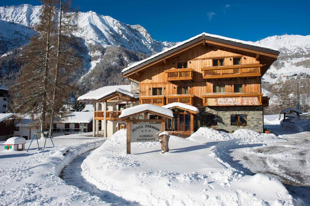 een groot houten gebouw in de sneeuw met een berg bij Albergo Punta Zerbion in Champoluc