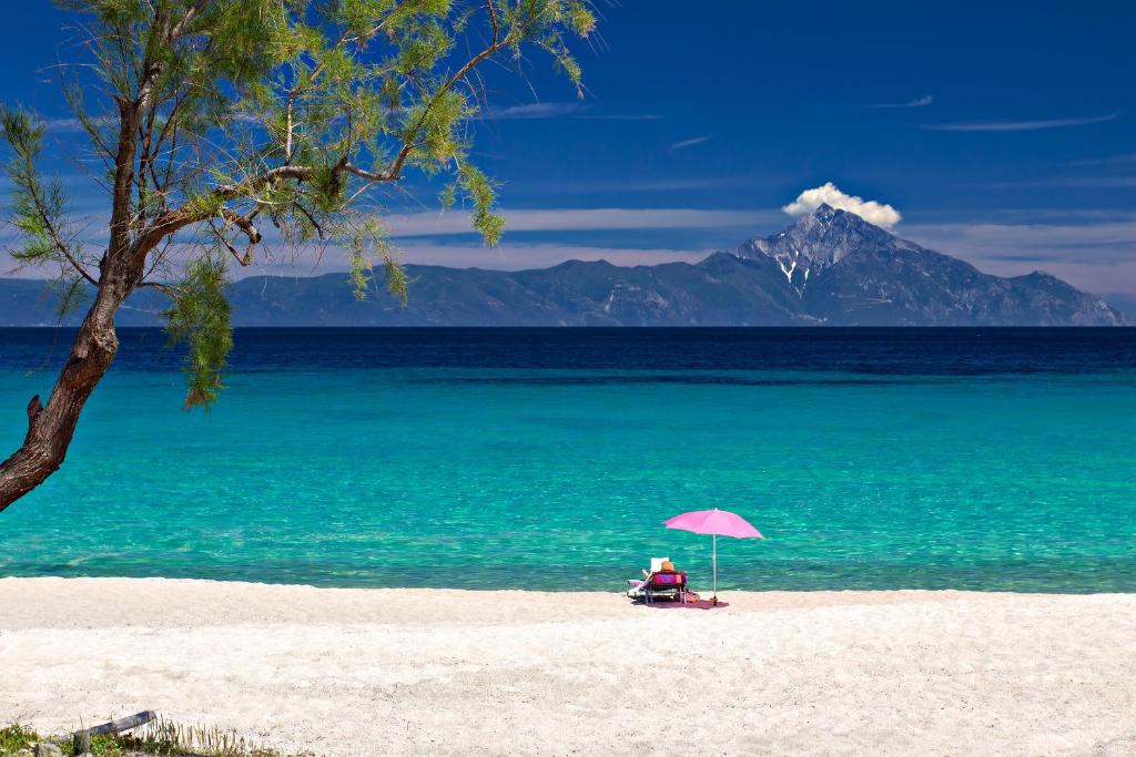 a person sitting in a chair under an umbrella on a beach at Armenistis Camping & Bungalows in Sarti