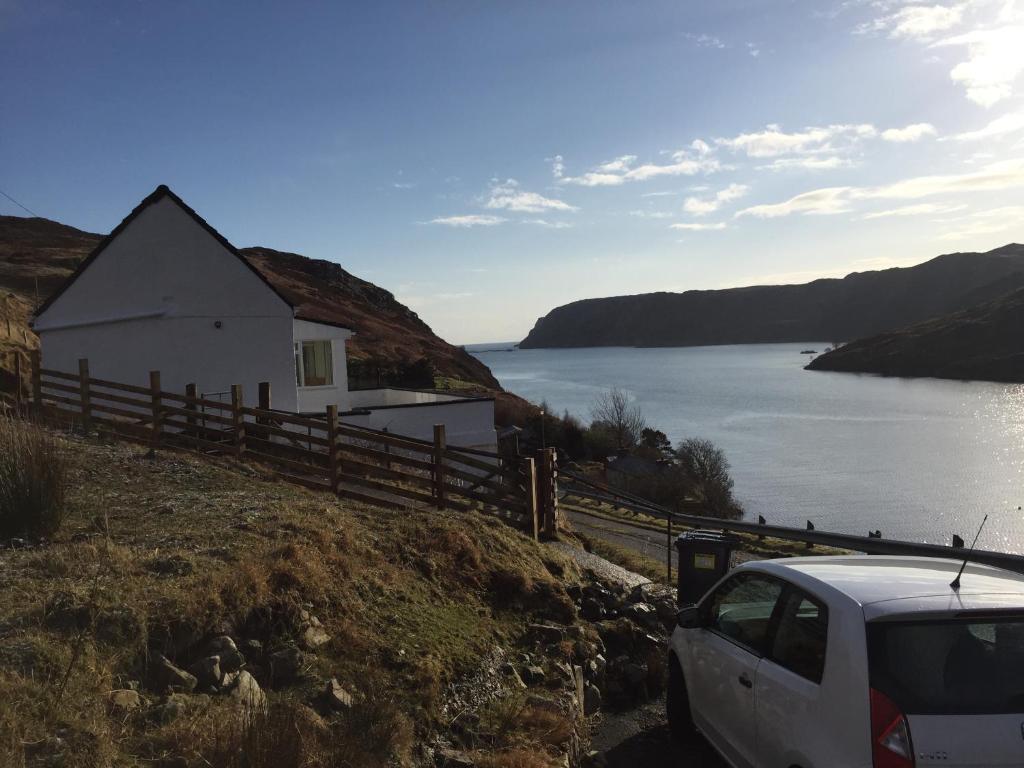 Ein weißes Haus auf einem Hügel neben einem Wasserkörper in der Unterkunft Sealoch Cottage in Breasclete