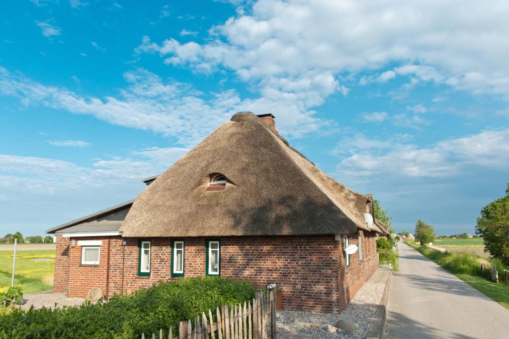 una casa con techo de paja y una valla delante en Reetdachhaus Moordeichperle en Nordstrand