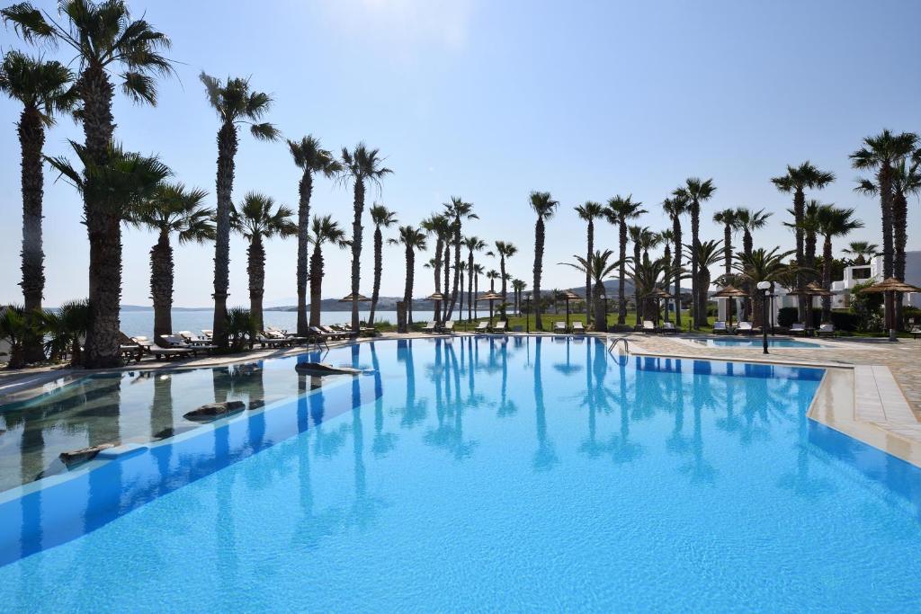 a large swimming pool with palm trees and the ocean at Astir Of Paros in Naousa