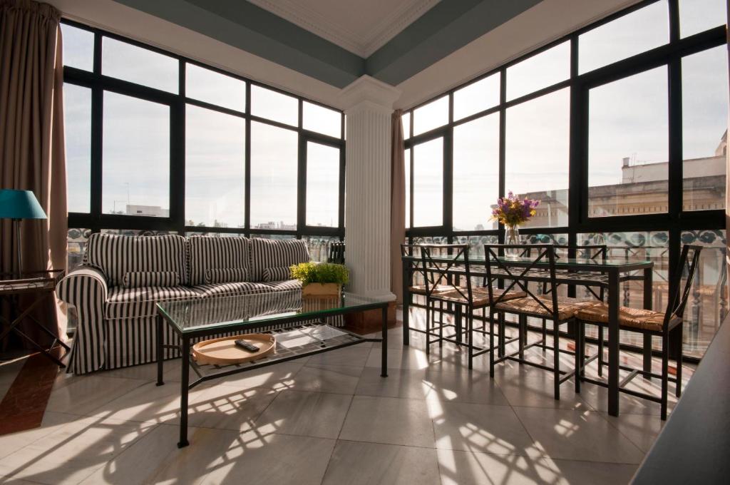 - un salon avec un canapé, des tables et des fenêtres dans l'établissement Apartamentos Avenida, à Séville