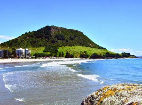 a beach with a hill in the middle of the ocean at Eleven_at_Mauao in Mount Maunganui
