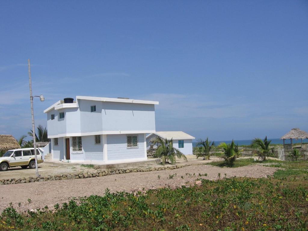 a white house with a car parked in front of it at Hostal Cabañas Vistamar in Crucita