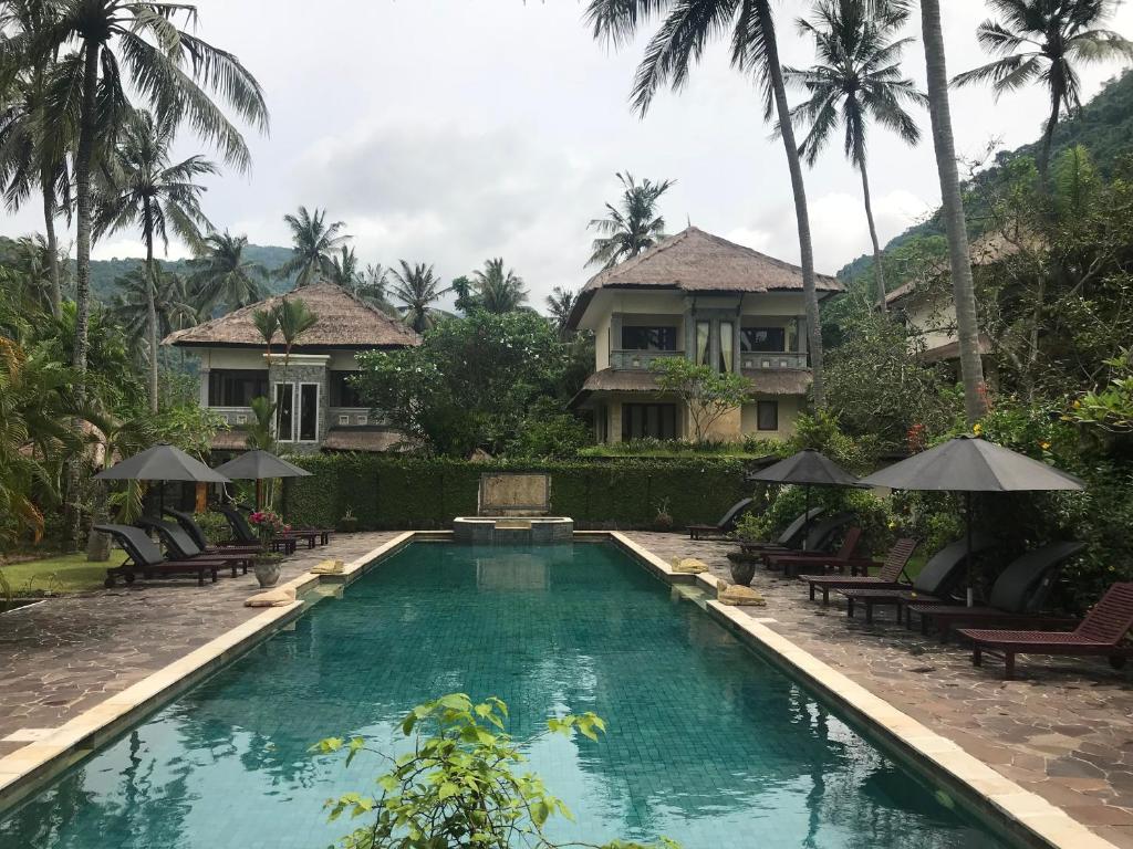 a swimming pool in front of a house with palm trees at Villa Serendah Senggigi in Senggigi 