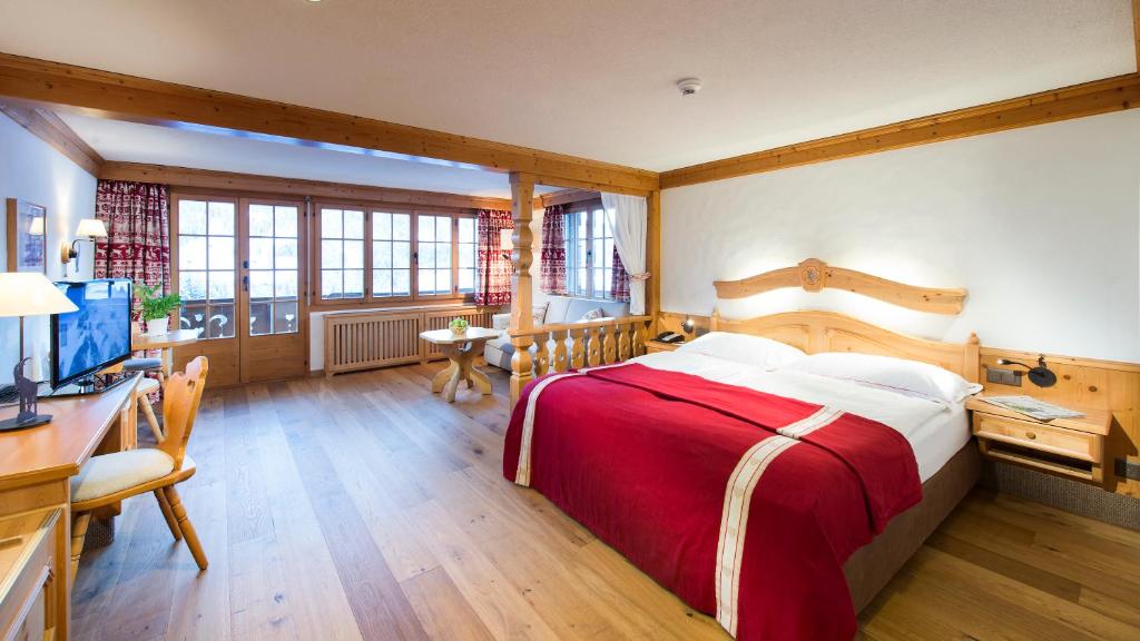 a bedroom with a bed and a desk and a television at Geniesserhotel Le Grand Chalet in Gstaad