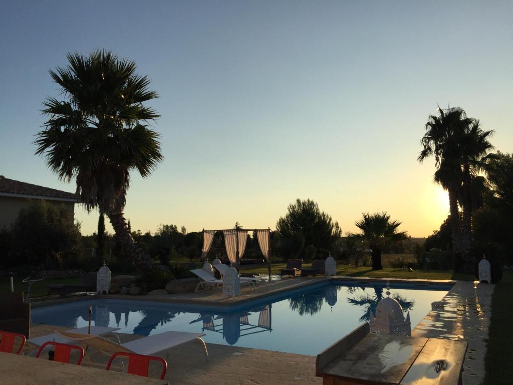 - une piscine avec des chaises et des palmiers et le coucher du soleil dans l'établissement Escapades Lointaines, à Perpignan
