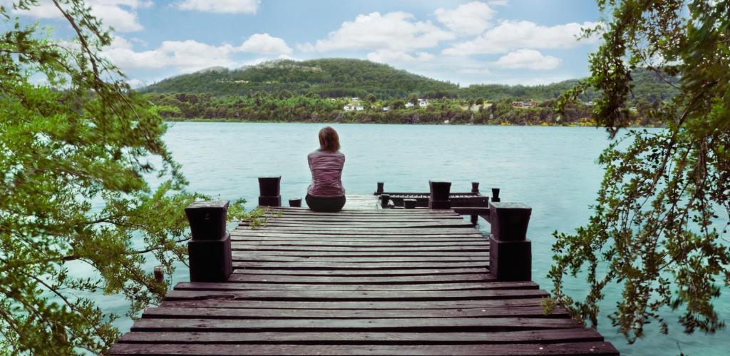 a woman sitting on a dock over a body of water at Casa Fischer del Lago in San Carlos de Bariloche