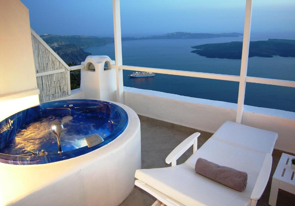 a bathroom with a tub and a chair and water at Aeolos Art & Eco Suites Adults Only in Imerovigli