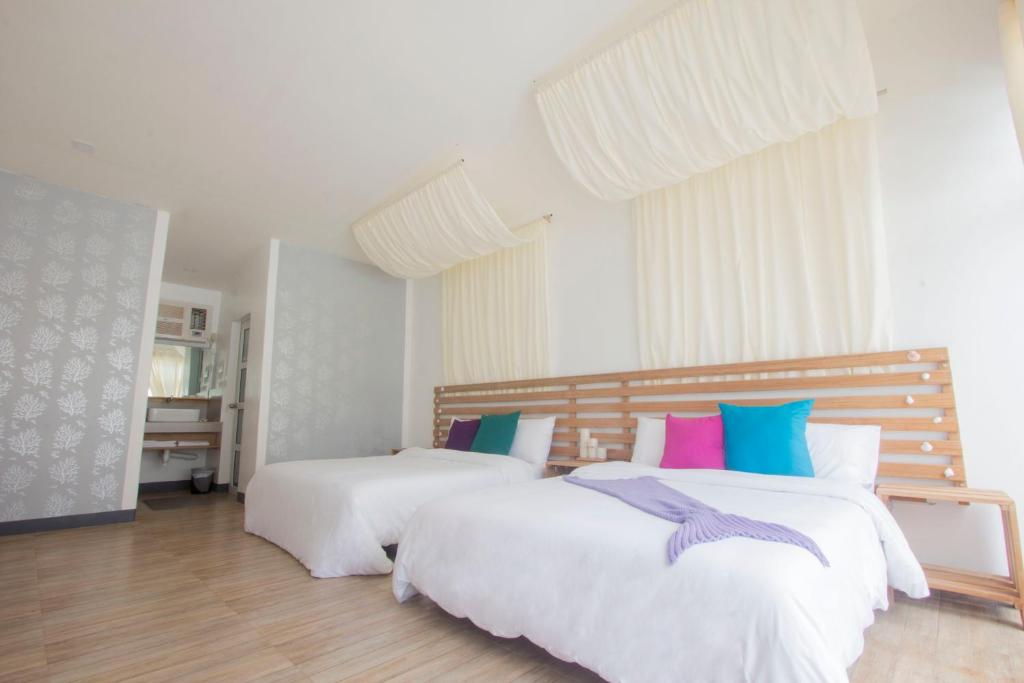 una camera con due letti con lenzuola bianche e cuscini colorati di L'Sirene Boutique Resort a Baler