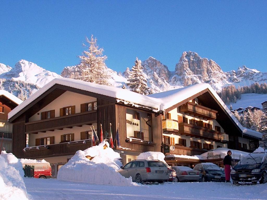 un lodge de ski avec des voitures garées dans la neige dans l'établissement Park Hotel Arnica, à Falcade