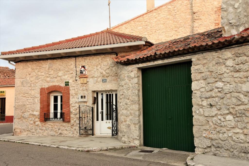 a stone building with a green door on a street at Casa Rural El Camino in Montemayor de Pililla