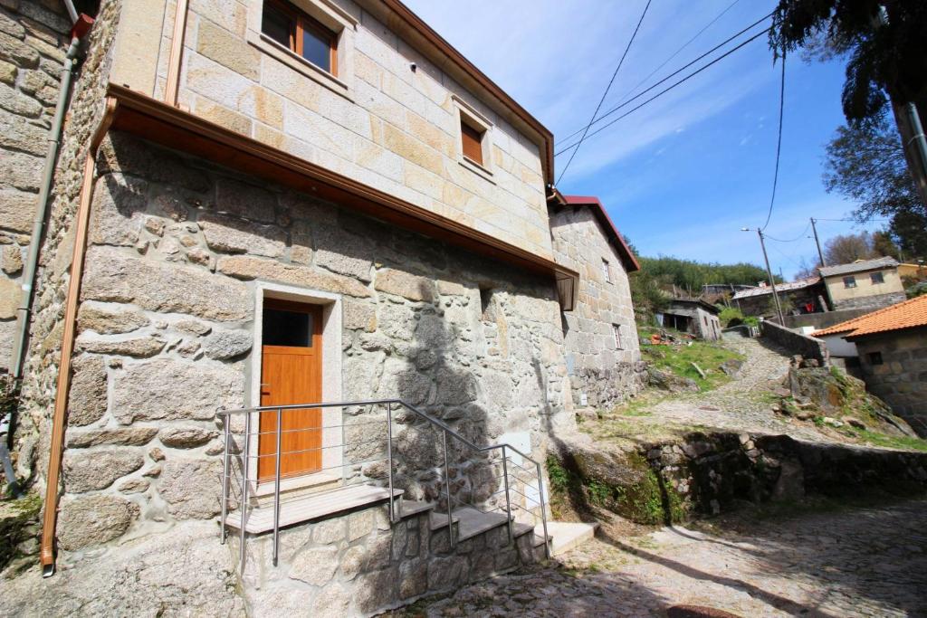 une vieille maison en pierre avec une porte orange dans une rue dans l'établissement Casa Joao Vilar, à Campo do Gerês