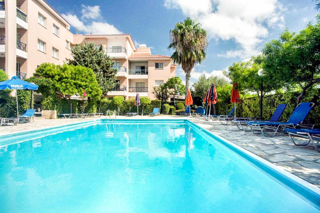 a swimming pool with chairs and umbrellas and a building at Pafia 3 Holiday Apartment in Paphos City