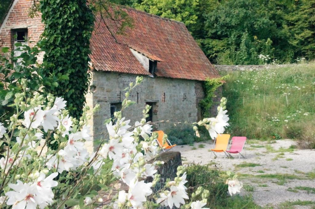 ein altes Haus mit Stühlen und Blumen davor in der Unterkunft Hotel du Moulin aux Draps in Desvres