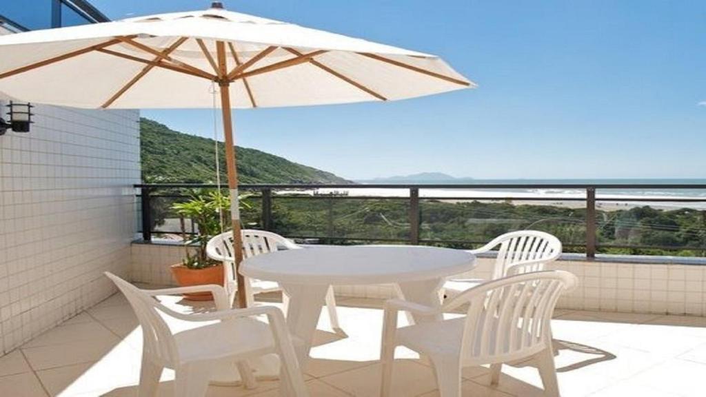 una mesa y sillas blancas y una sombrilla en el balcón en Lindo apartamento de cobertura de frente para o mar com piscina privativa!, en Florianópolis