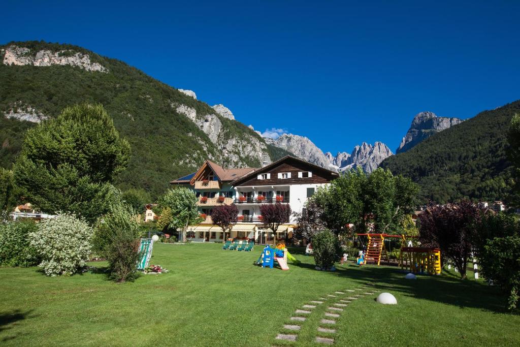 a house on a lawn with a playground in front of a mountain at Garden Hotel Bellariva in Molveno